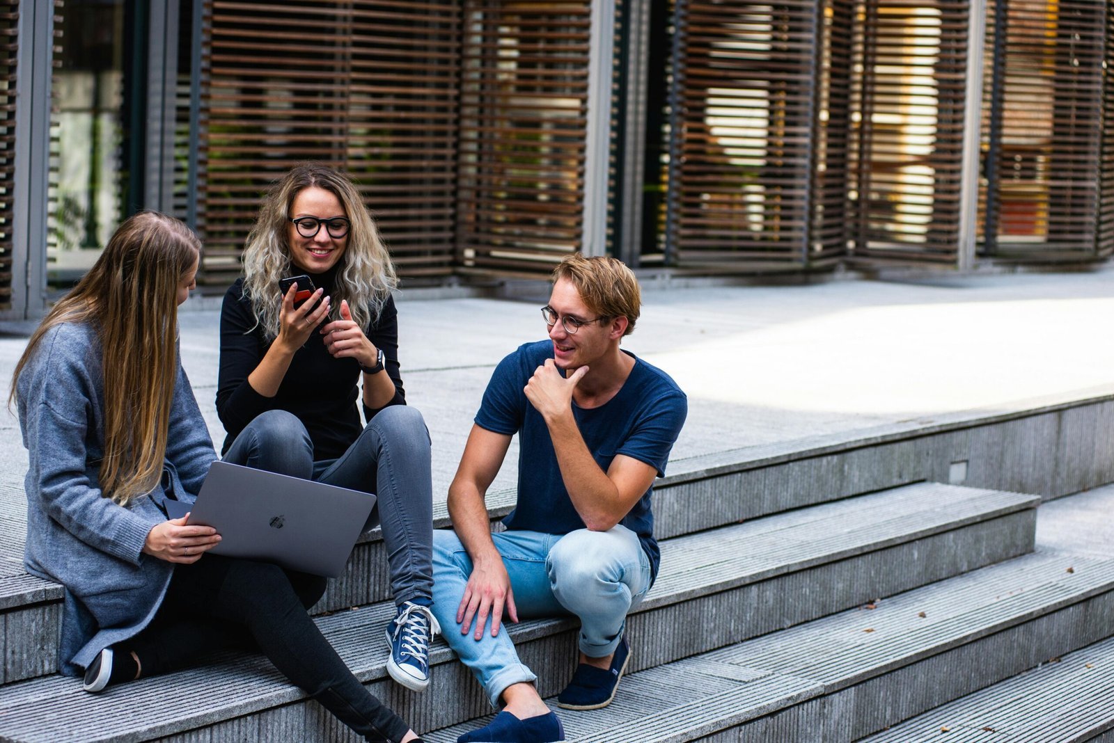 Young adults chatting and using tech on campus steps.