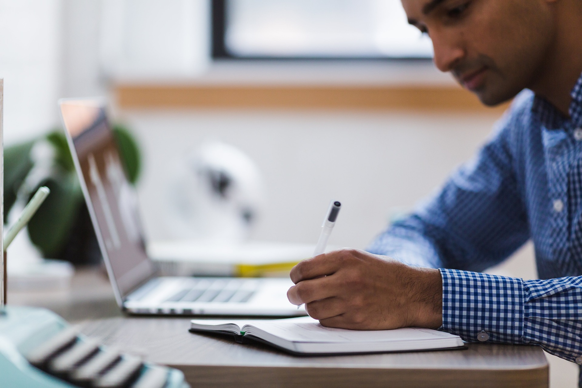 Man writing in notebook beside laptop on desk