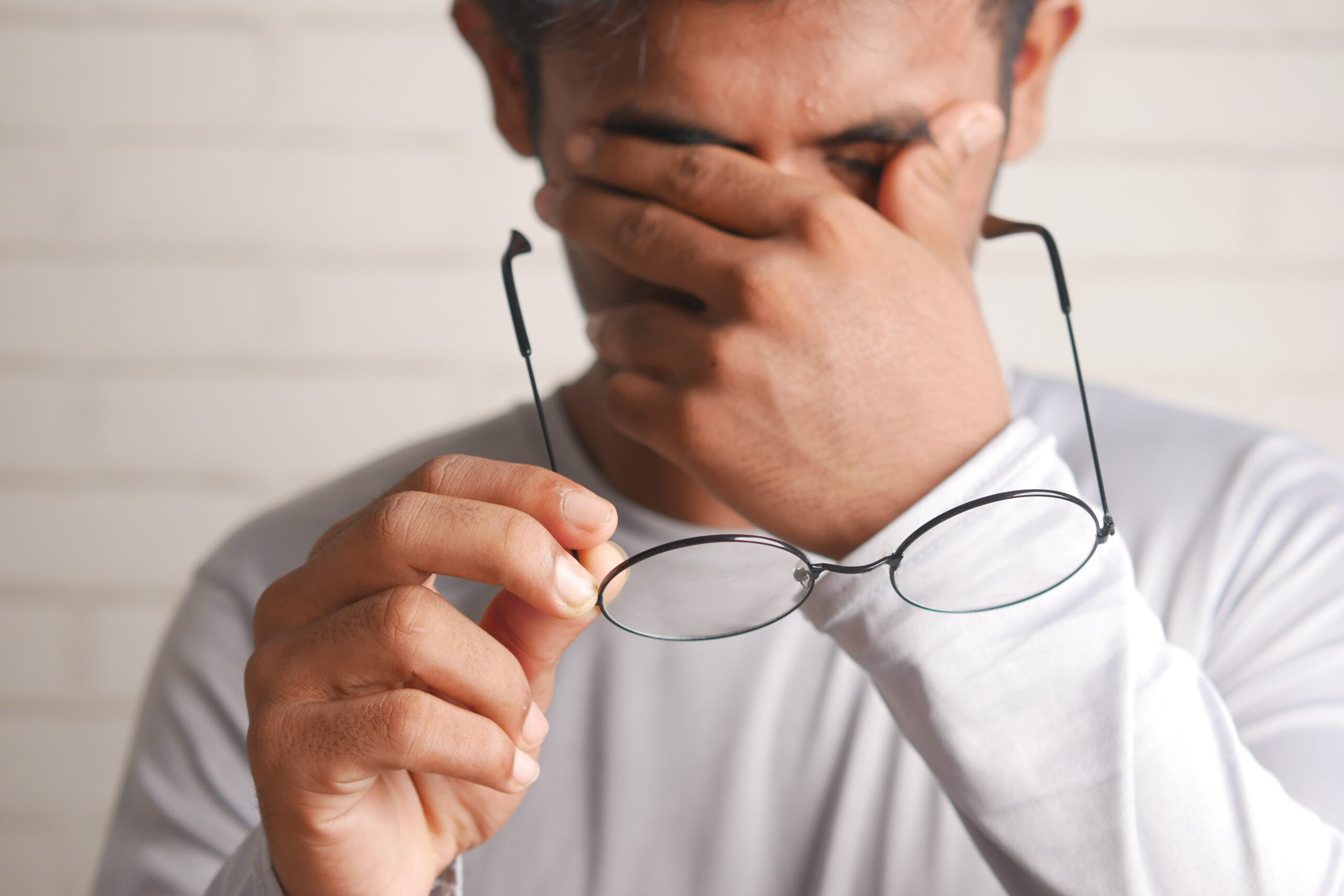 Man holding glasses, covering face with hand