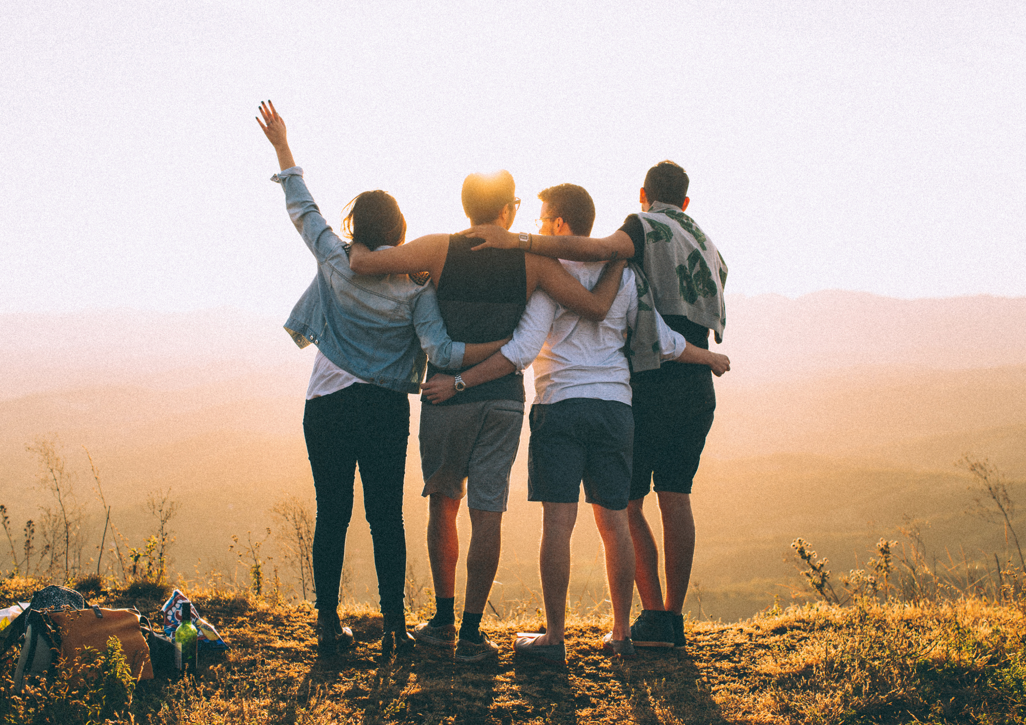Friends embracing on sunny hilltop at sunset