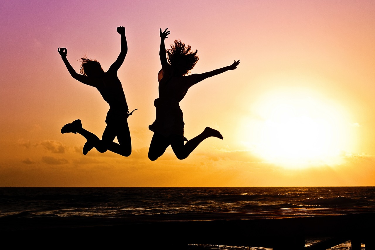 Two people jumping joyfully on beach at sunset