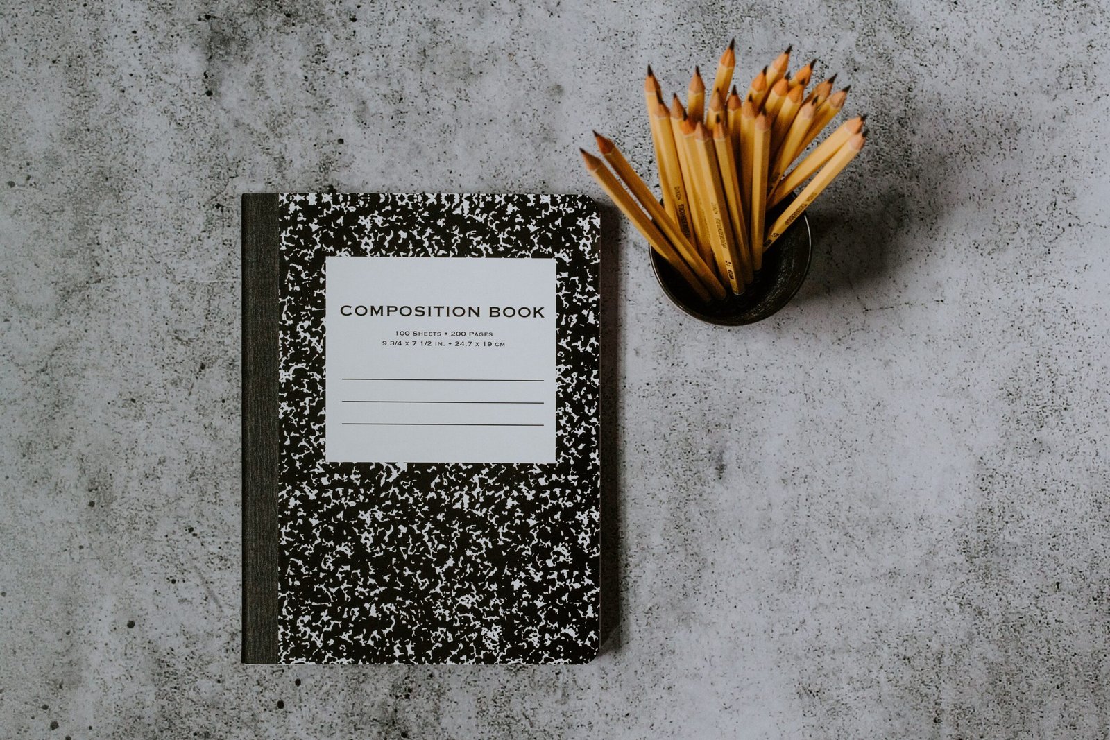 Composition book with pencils on textured gray surface