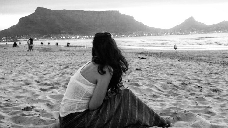 Woman sitting on beach facing mountain at sunset